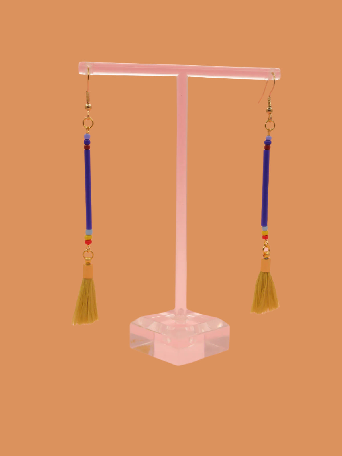 Long bead stick dangle earrings with blue glass tube beads & contrasting seed beads in blue, red & yellow. Paired with a chartreuse cotton tassel and hung from gold plated nickel free ear wires