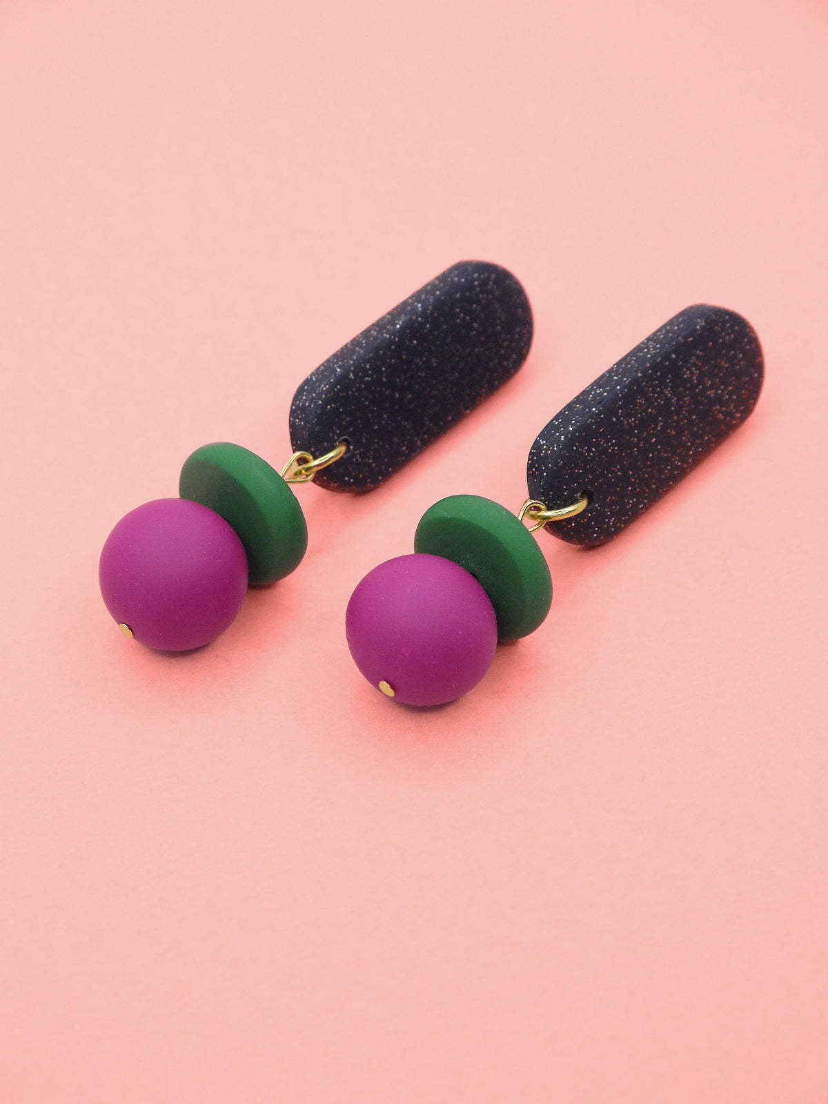 Pair of earrings with black, green, and pink beads on a pink background