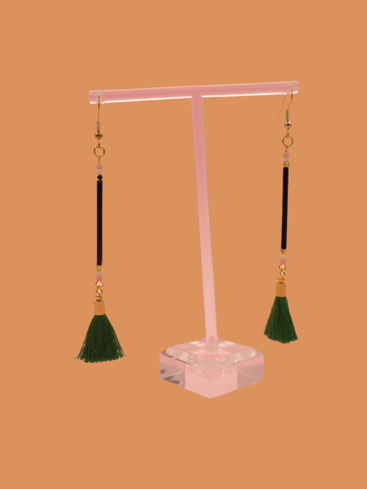 Long delicate bead stick dangle earrings with black glass tube beads & contrasting seed beads in pink & white. Paired with a green cotton tassel & hung from gold plated nickel free ear wires