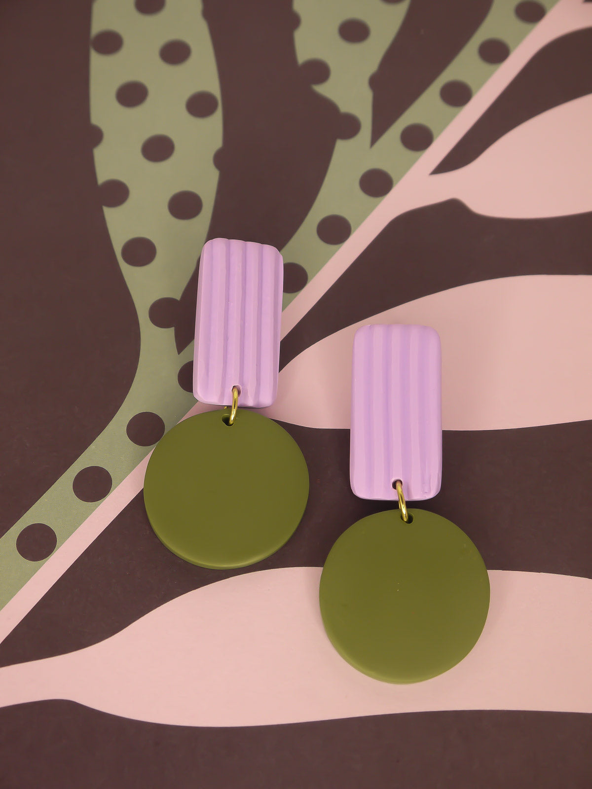 Pair of geometric earrings with purple and green colours on a patterned background
