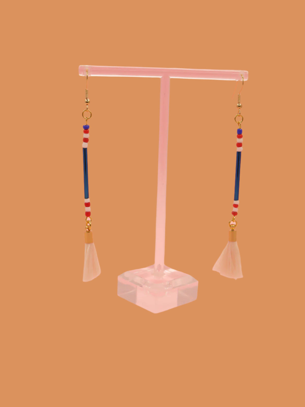 Lightweight delicate long beaded dangle earrings with a blue metallic tube bead and contrasting seed beads in red, white & blue, paired with a white cotton tassel. Hung from gold plated nickel free ear wires.