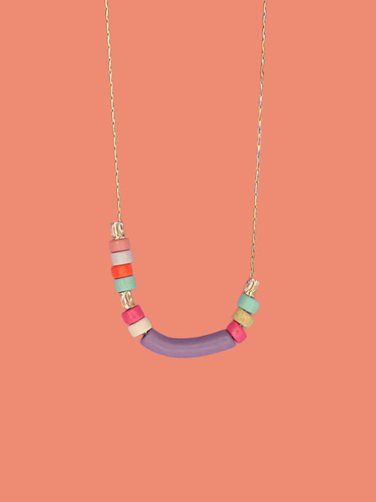 Dainty beaded ceramic necklace with a lilac curved bar bead, surrounded by textured brass tube beads and colourful ceramic beads in pink, turquoise, orange & white. Hung from a gold plated snake chain.