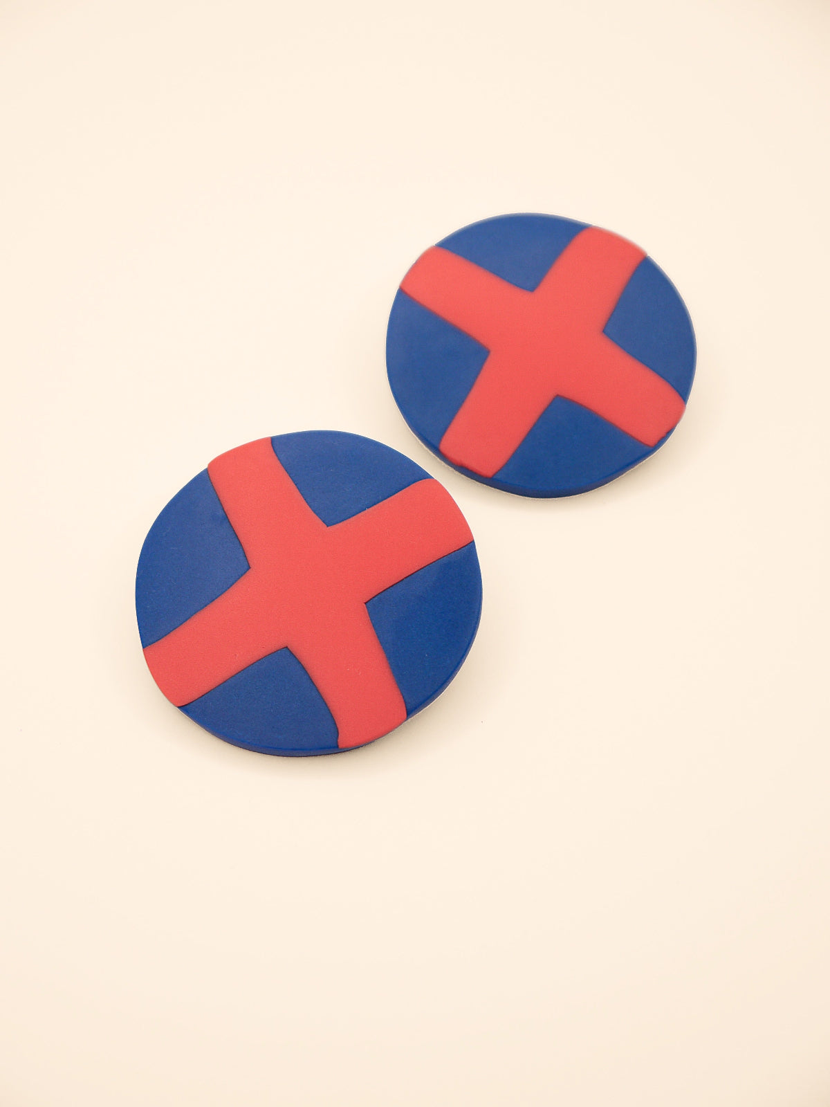 Two round blue stud earrings with red 'X' design on a beige background
