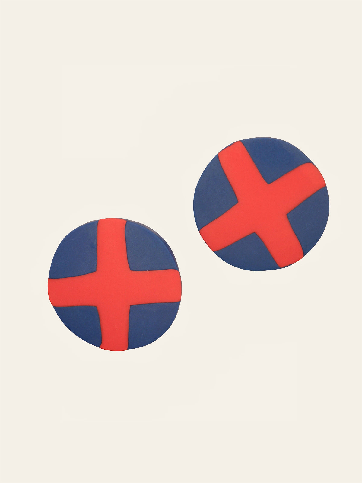 Two round blue stud earrings with red 'X' design on a beige background