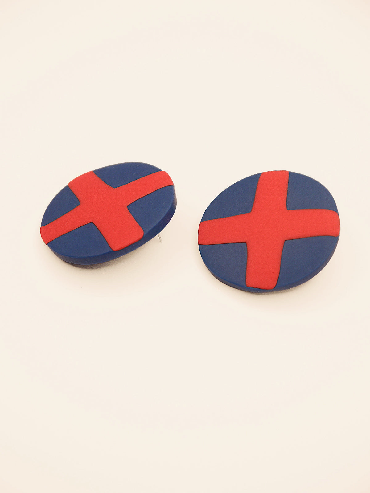 Two round blue stud earrings with red 'X' design on a beige background