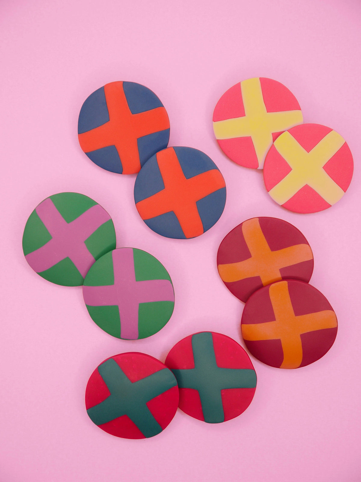 Colourful round geometric stud earrings with cross patterns on a pink background