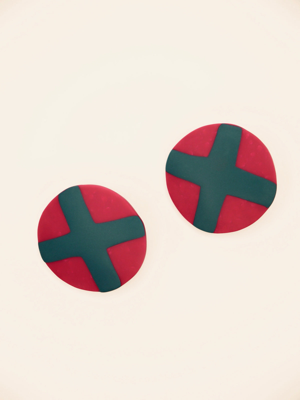 Fuchsia studs with green cross geometric earrings on a beige background
