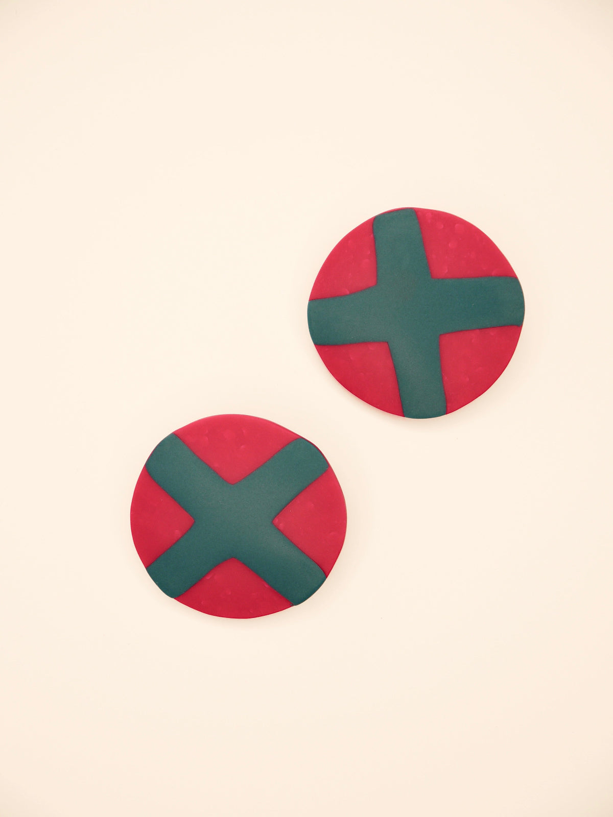 Fuchsia studs with green cross geometric earrings on a beige background