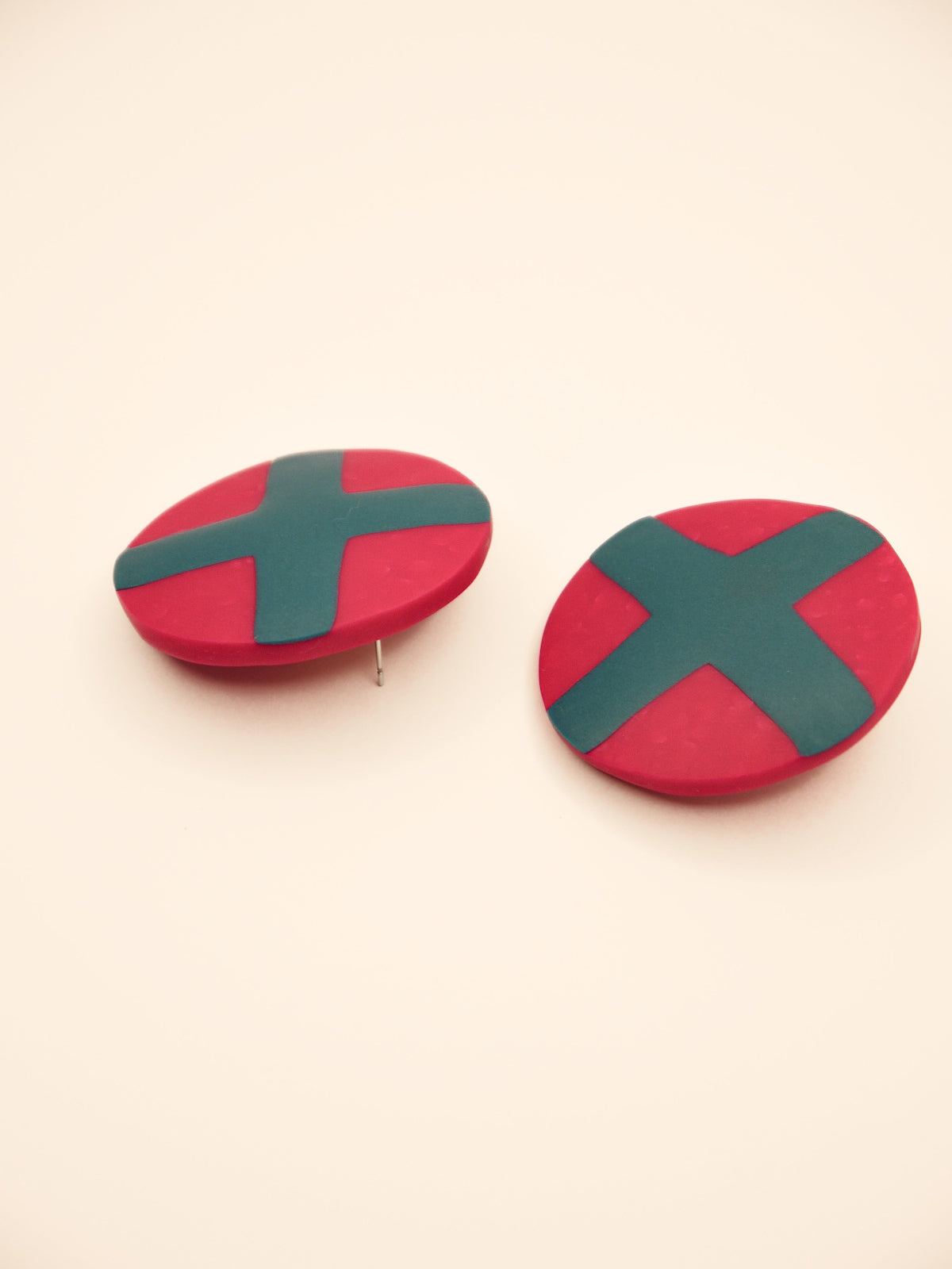 Fuchsia studs with green cross geometric earrings on a beige background