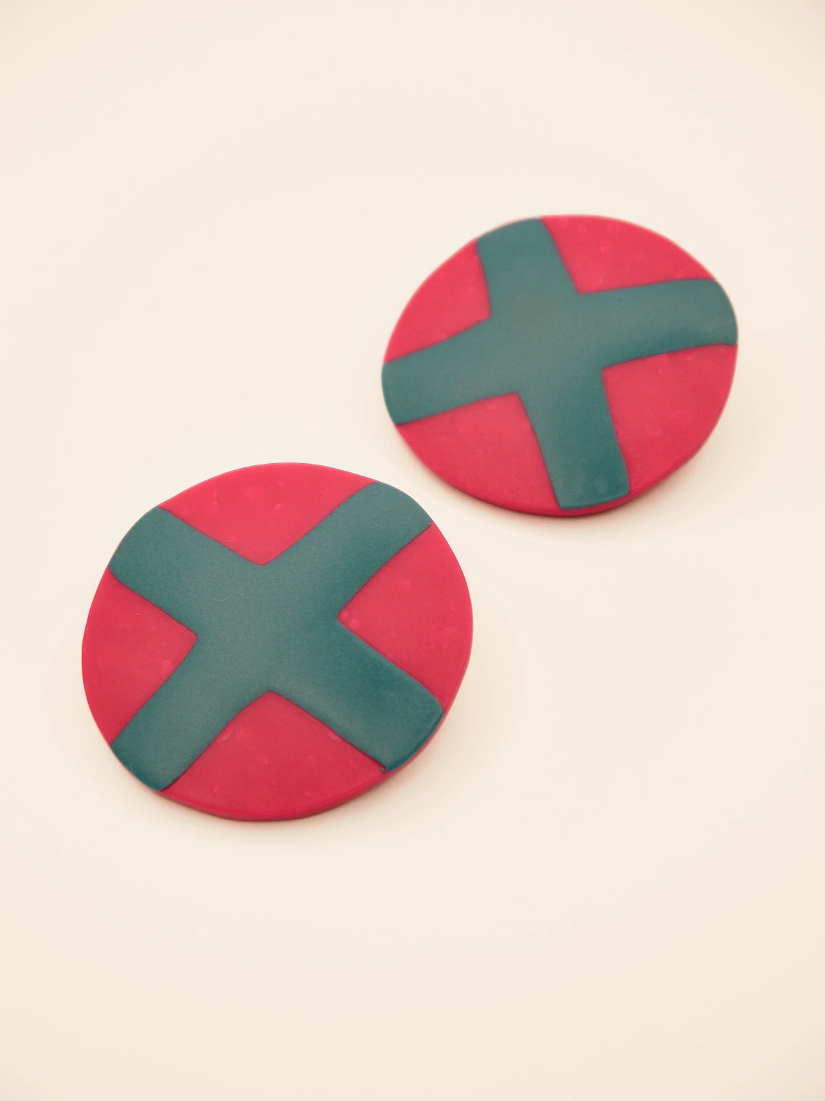 Fuchsia studs with green cross geometric earrings on a beige background