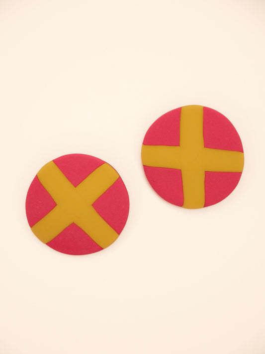 Two round pink stud earrings with yellow 'X' design on a beige background