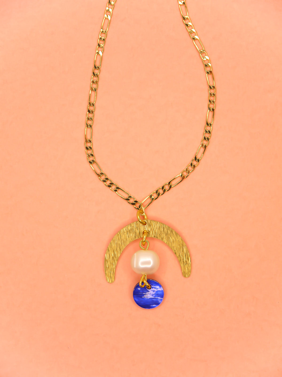 Geometric lightweight pendant necklace with a textured brass arch semi circle with a pearl and blue round shell disk hung from the arch on a faceted gold curb chain with extender.