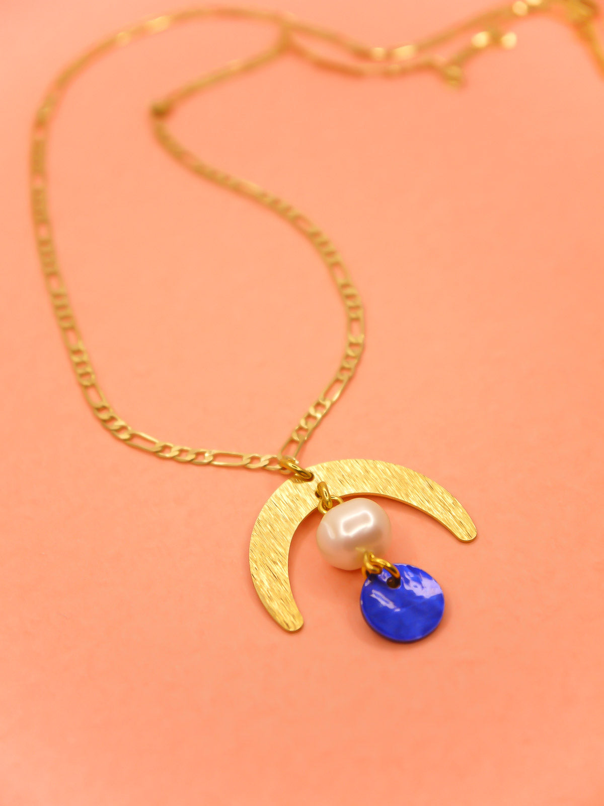 Geometric lightweight pendant necklace with a textured brass arch semi circle with a pearl and blue round shell disk hung from the arch on a faceted gold curb chain with extender.