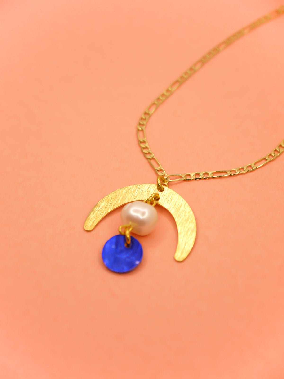 Geometric lightweight pendant necklace with a textured brass arch semi circle with a pearl and blue round shell disk hung from the arch on a faceted gold curb chain with extender.