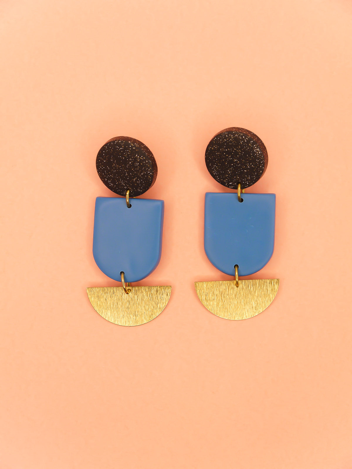 Geometric polymer clay dangle earrings with a black glitter circle stud, connected to a blue arch & a textured brass semi circle 