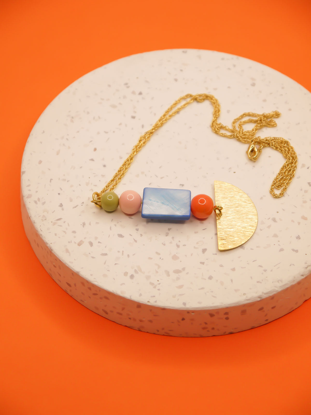 Lightweight geometric necklace featuring a textured brass semi circle charm with glass beads in orange, pink & green with a blue mother of pearl square bead. Hung from 24k gold plated cable chain.