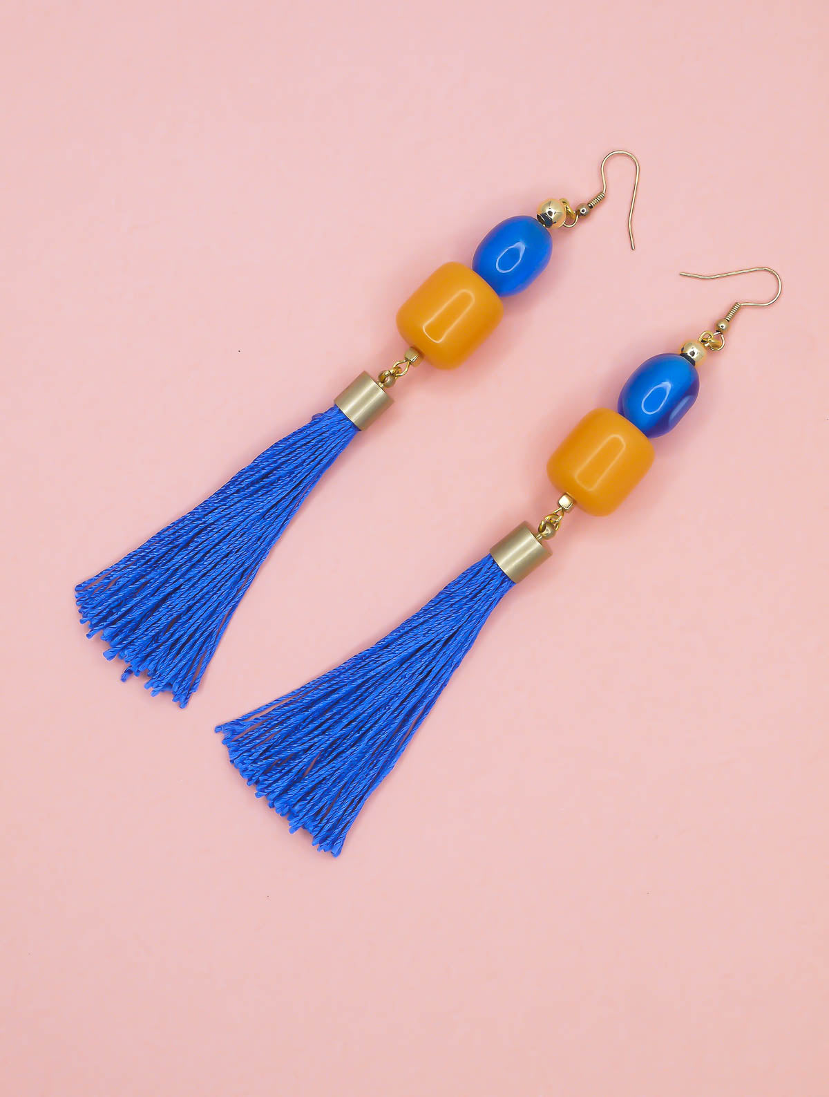 Blue tassel earrings with blue, orange and gold beads on a pink background