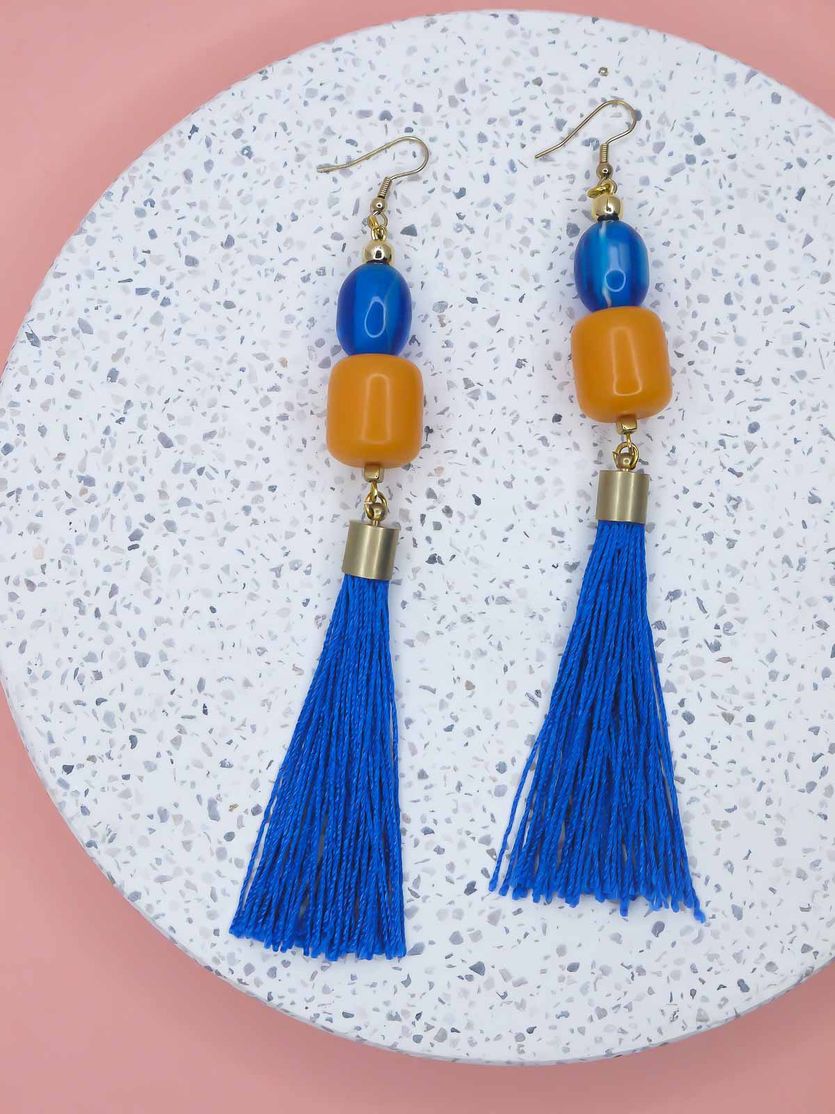 Pair of earrings with blue tassels and colorful beads on a textured surface.