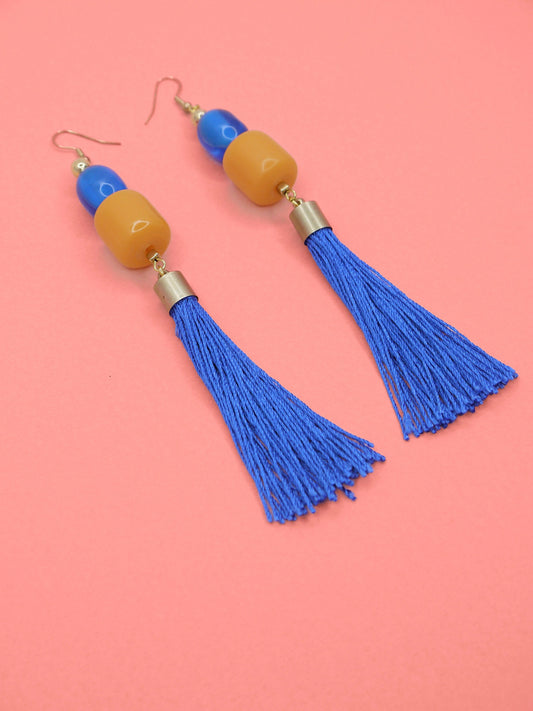 Colourful blue tassel earrings with blue & orange beads on a pink background