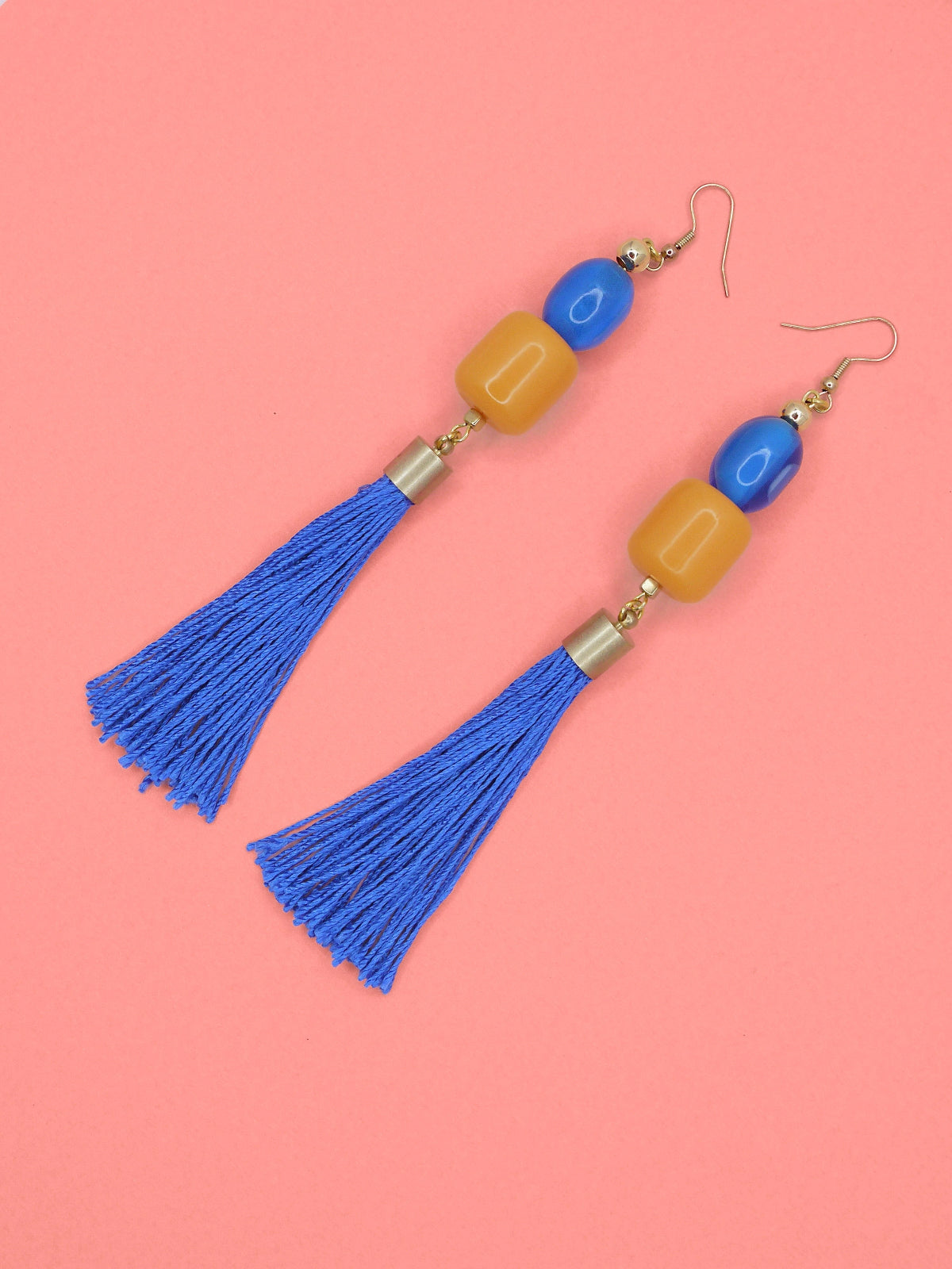 Colourful blue tassel earrings with blue & orange beads on a pink background