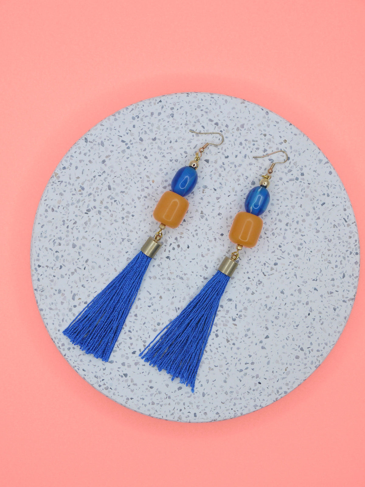 Colourful blue tassel earrings with blue & orange beads on a terrazzo circle & a pink background