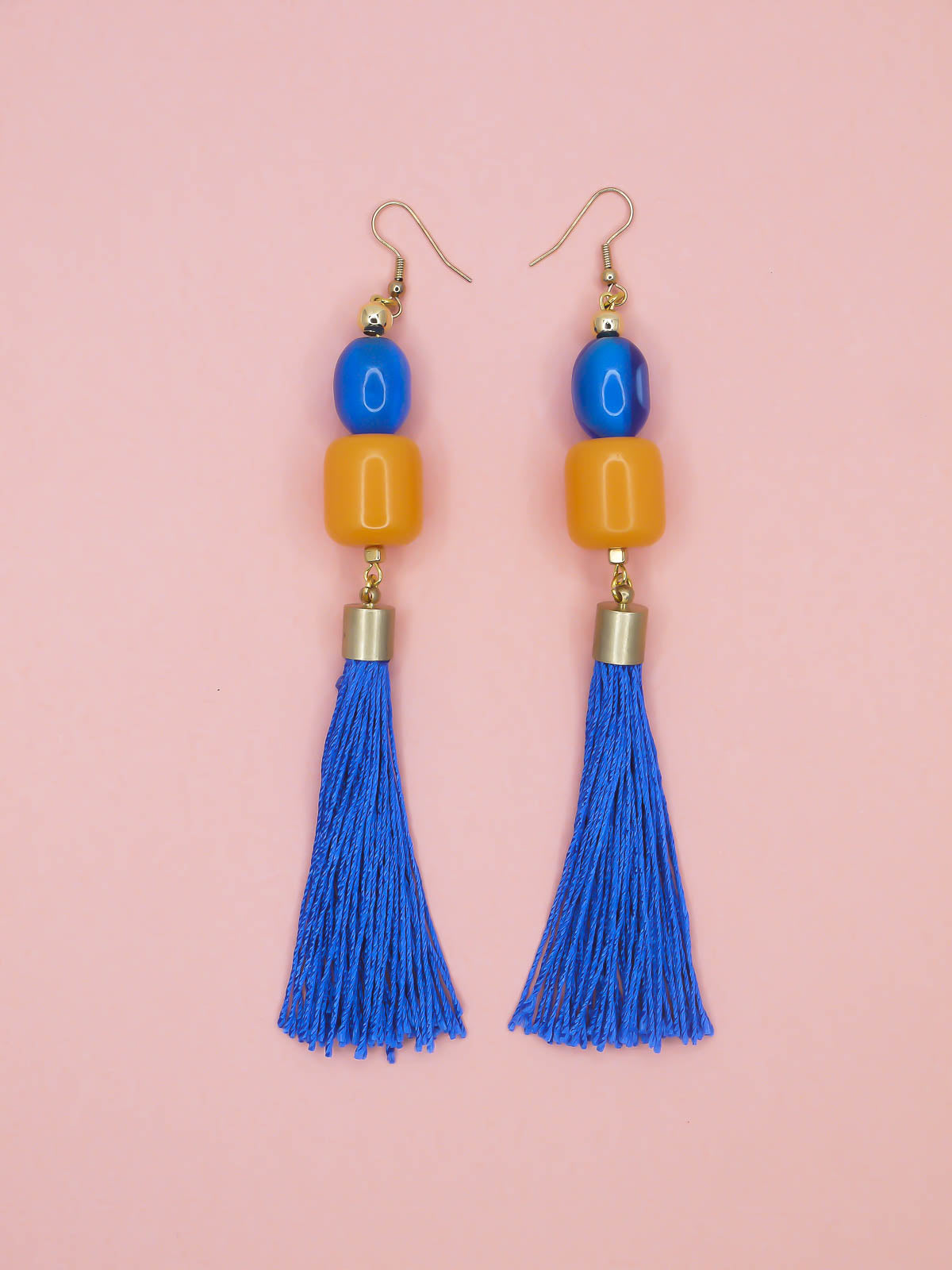 Colourful blue tassel earrings with blue & orange beads on a pink background