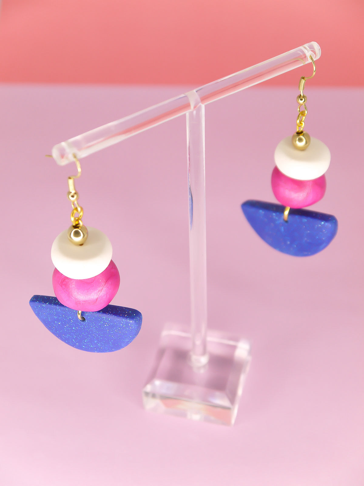 Geometric dangle statement earrings with a blue glitter semi circle, hand rolled beads in pink metallic and white glitter with a brass ball bead hung from gold plated ear wires