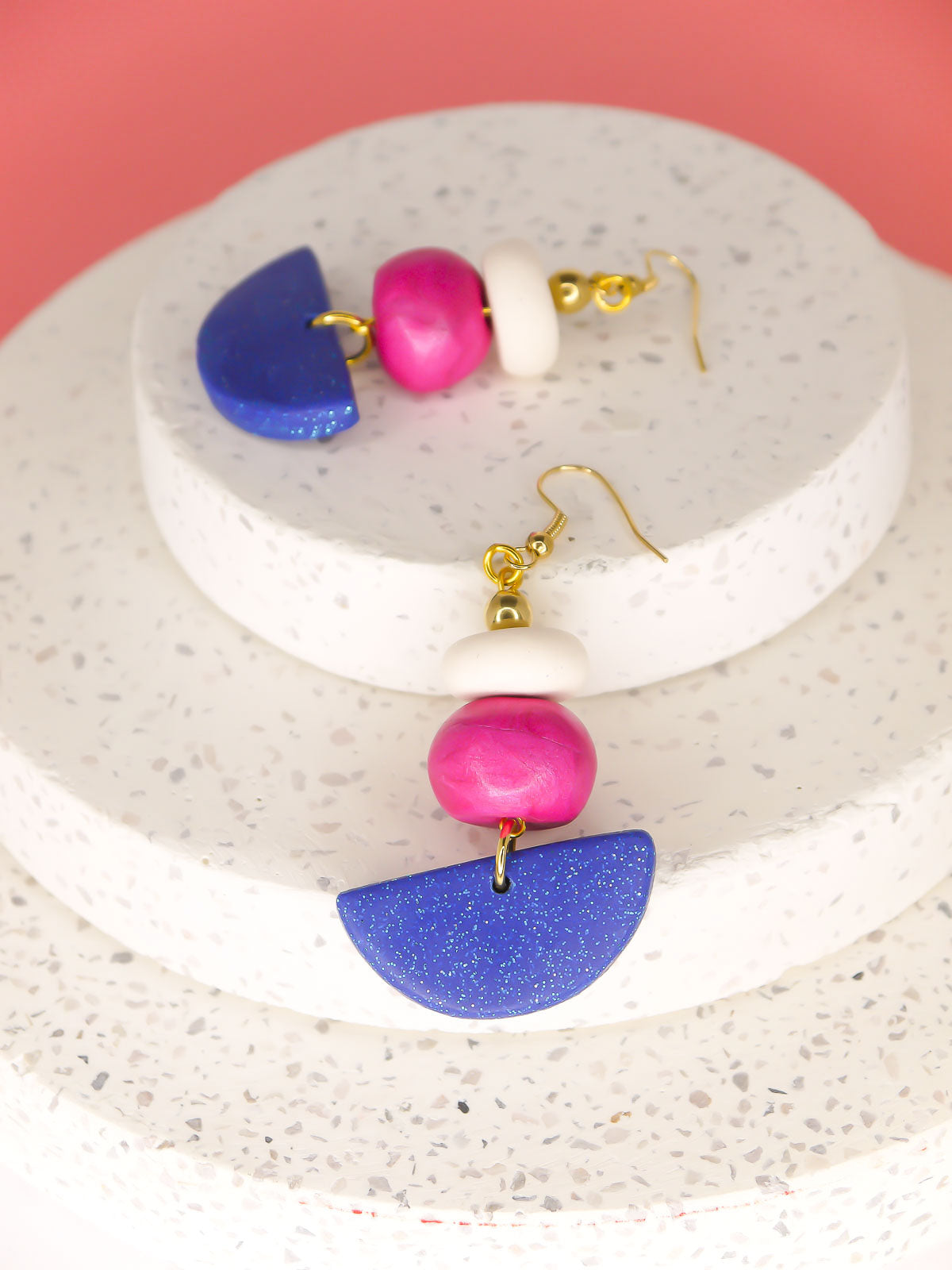 Geometric dangle statement earrings with a blue glitter semi circle, hand rolled beads in pink metallic and white glitter with a brass ball bead hung from gold plated ear wires