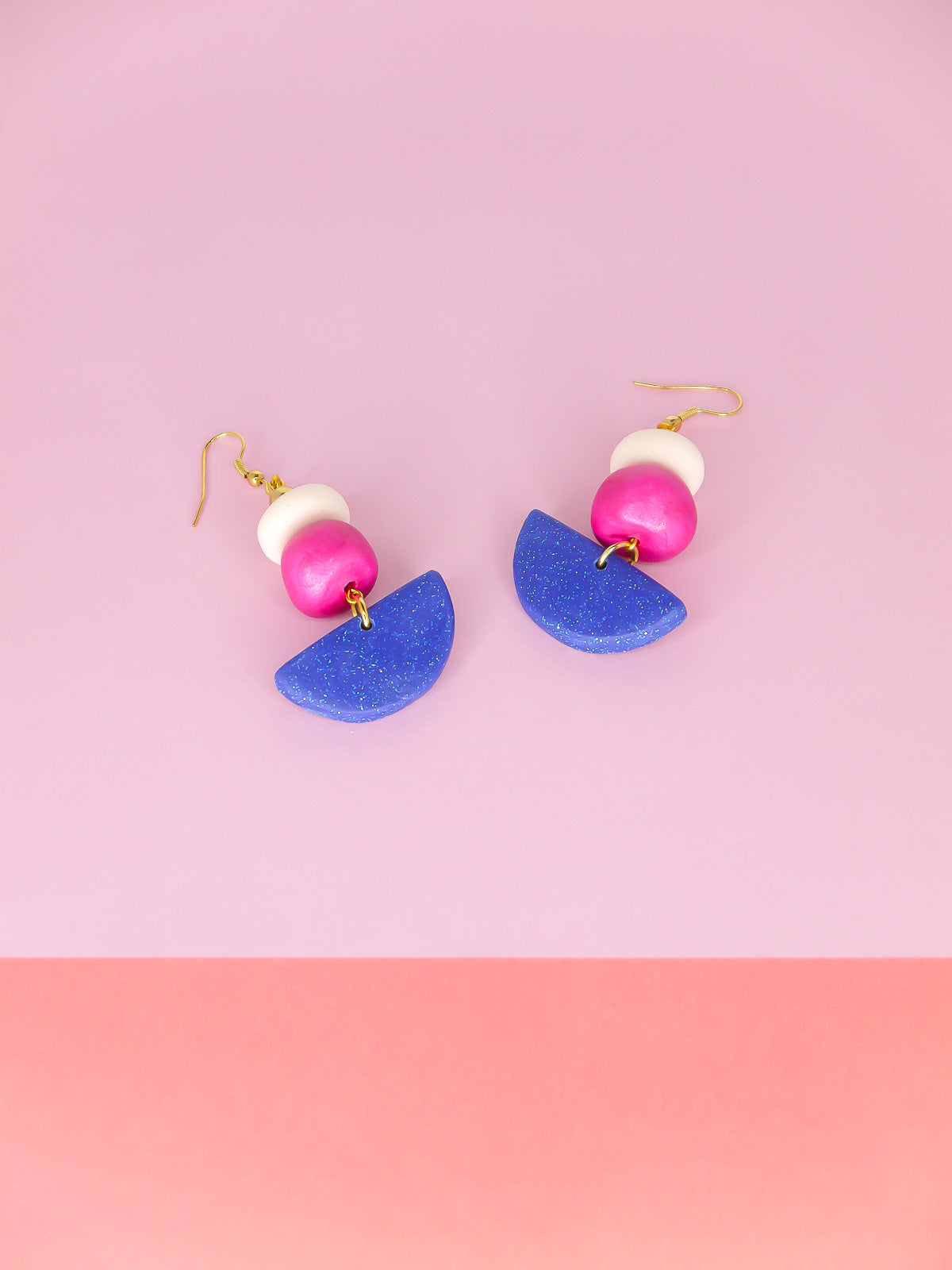 Geometric dangle statement earrings with a blue glitter semi circle, hand rolled beads in pink metallic and white glitter with a brass ball bead hung from gold plated ear wires