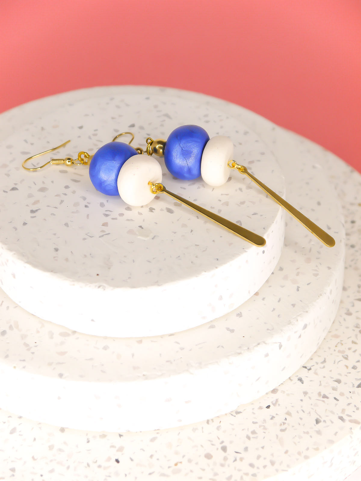 Metallic bead dangle earrings with two hand rolled metallic beads in blue and white glitter with a brass stick charm, hung from gold plated ear wires