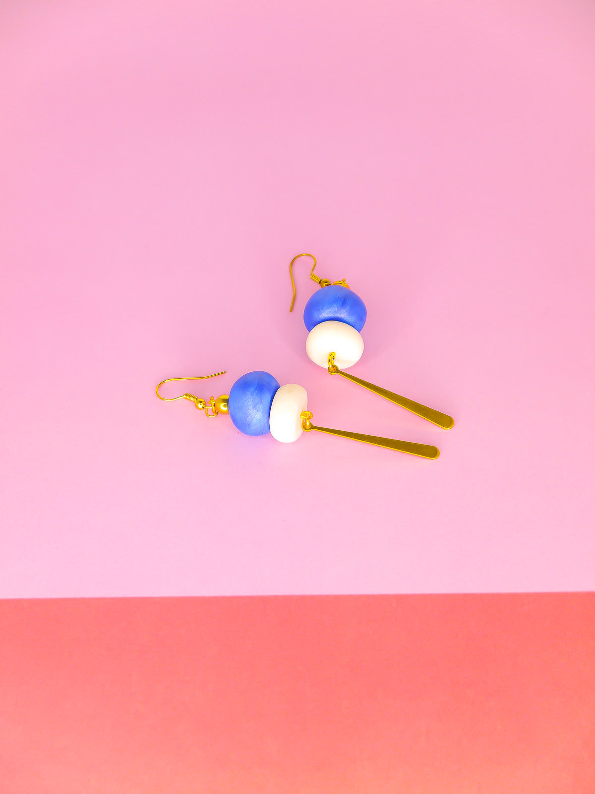 Metallic bead dangle earrings with two hand rolled metallic beads in blue and white glitter with a brass stick charm, hung from gold plated ear wires