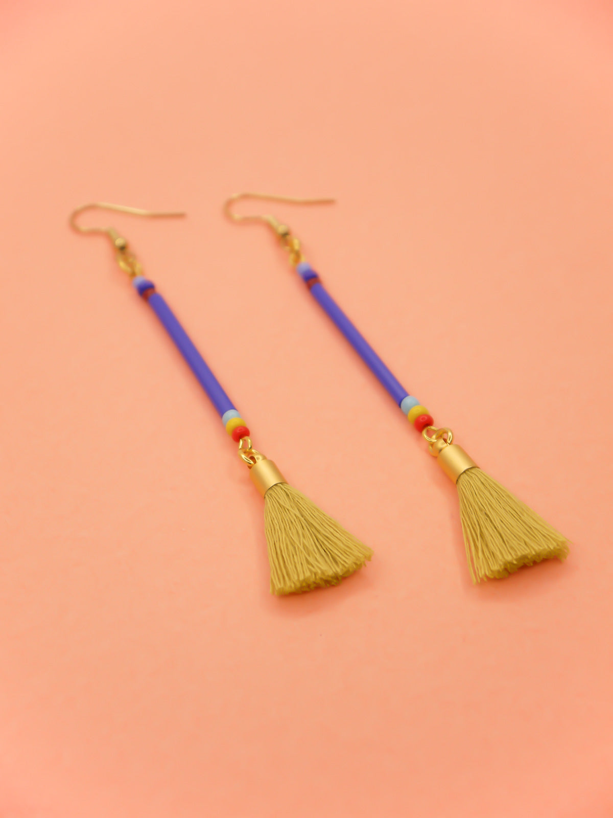 Long bead stick dangle earrings with blue glass tube beads & contrasting seed beads in blue, red & yellow. Paired with a chartreuse cotton tassel and hung from gold plated nickel free ear wires