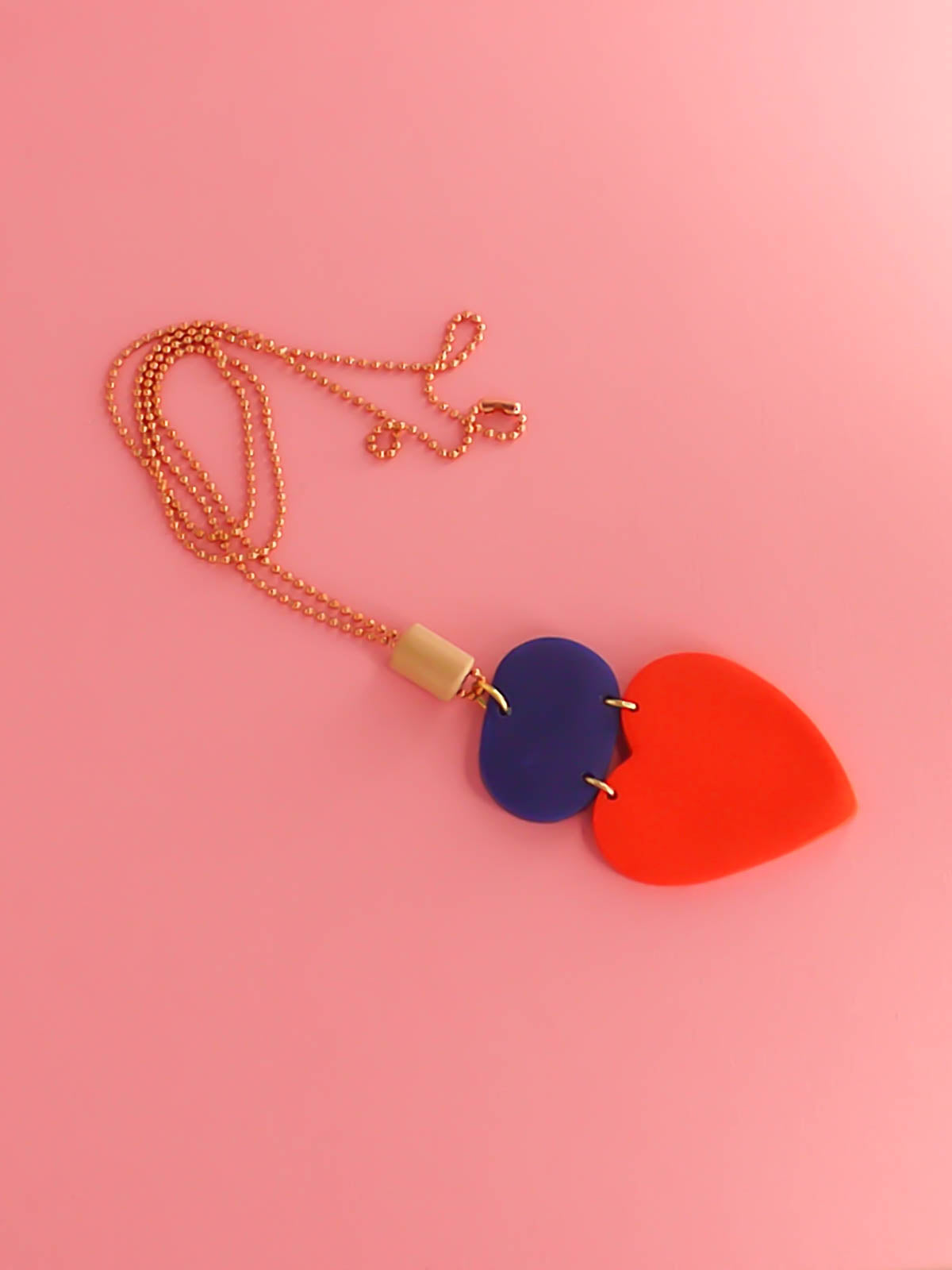 Colour block heart pendant necklace made out of lightweight polymer clay with a red heart, connected to a cobalt blue rectangle and a wooden tube bead hung on a copper ball chain