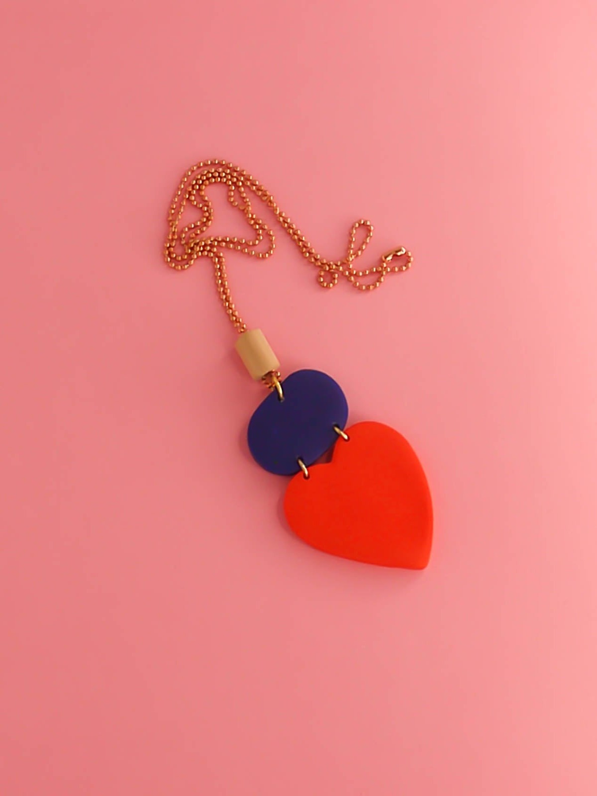 Colour block heart pendant necklace made out of lightweight polymer clay with a red heart, connected to a cobalt blue rectangle and a wooden tube bead hung on a copper ball chain