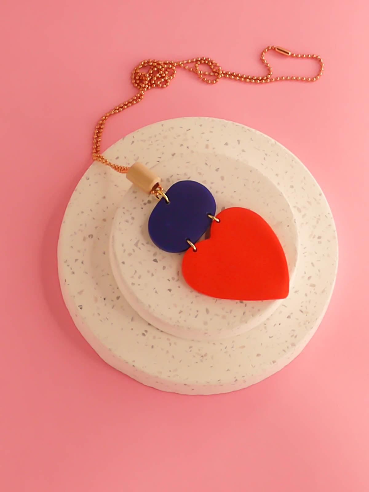 Colour block heart pendant necklace made out of lightweight polymer clay with a red heart, connected to a cobalt blue rectangle and a wooden tube bead hung on a copper ball chain