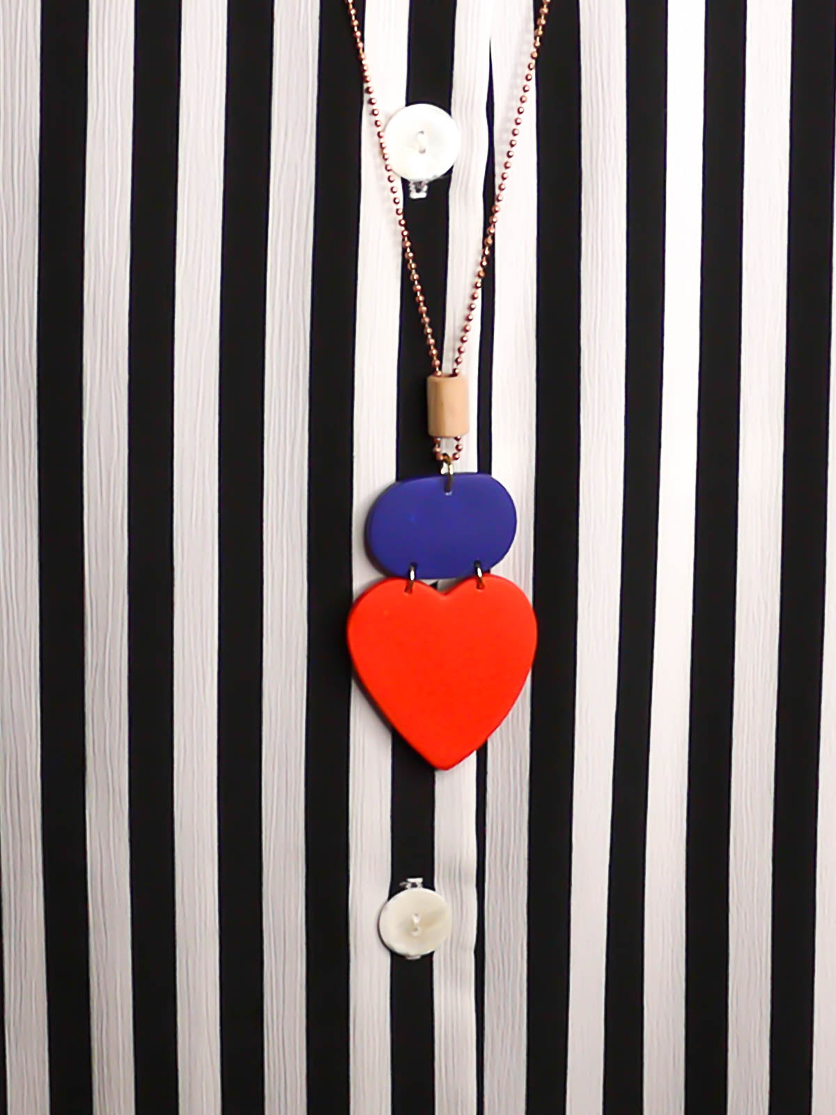 Colour block heart pendant necklace made out of lightweight polymer clay with a red heart, connected to a cobalt blue rectangle and a wooden tube bead hung on a copper ball chain