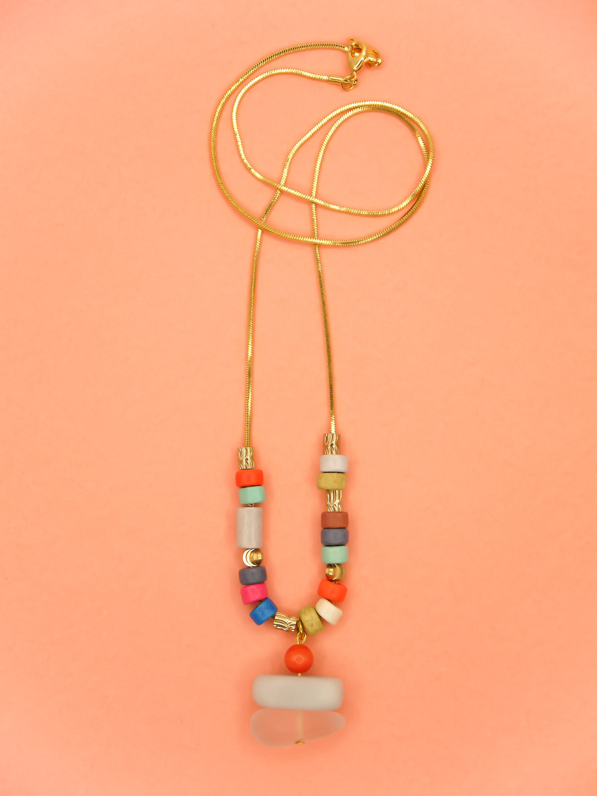 Crystal gemstone pendant necklace with a frosted crystal bead, stacked with an amazonite and coral bead, featuring multi coloured ceramic tube beads with textured brass tube beads hung on a gold plated snake chain