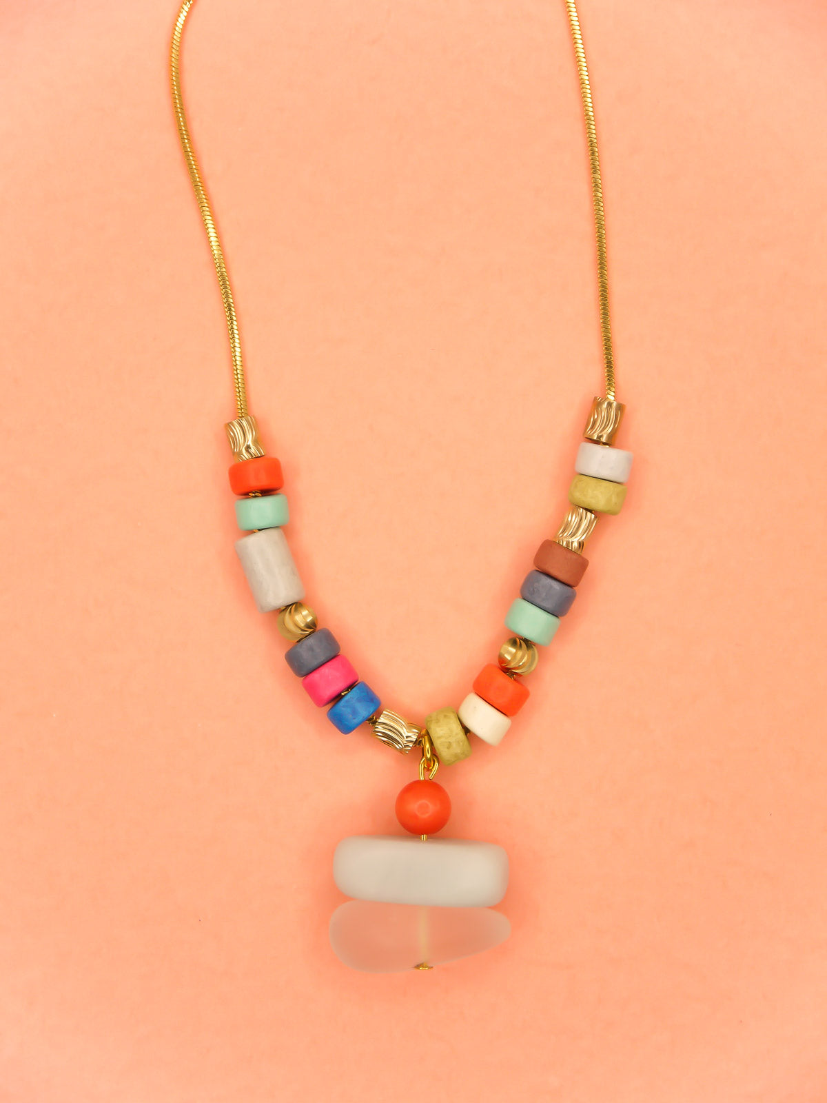 Crystal gemstone pendant necklace with a frosted crystal bead, stacked with an amazonite and coral bead, featuring multi coloured ceramic tube beads with textured brass tube beads hung on a gold plated snake chain