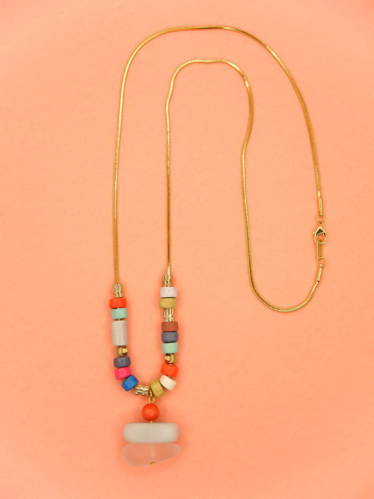 Crystal gemstone pendant necklace with a frosted crystal bead, stacked with an amazonite and coral bead, featuring multi coloured ceramic tube beads with textured brass tube beads hung on a gold plated snake chain