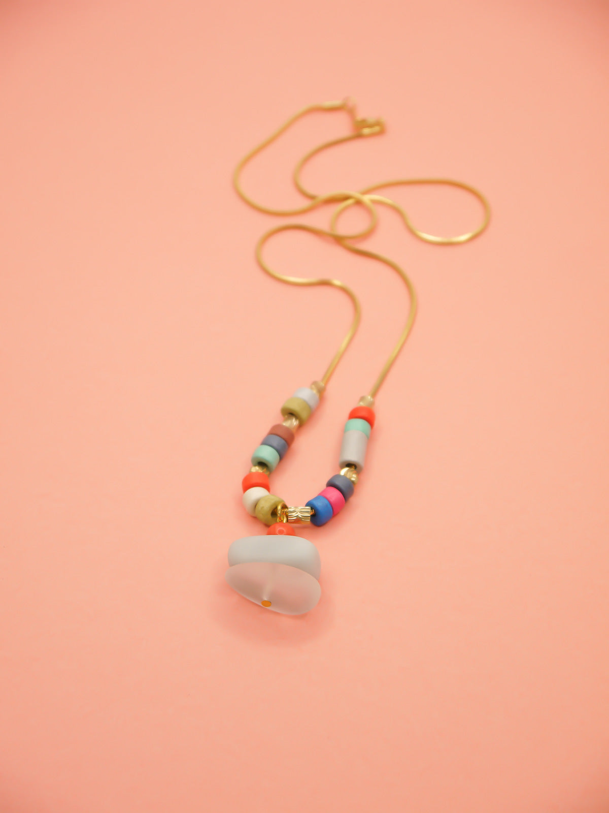 Crystal gemstone pendant necklace with a frosted crystal bead, stacked with an amazonite and coral bead, featuring multi coloured ceramic tube beads with textured brass tube beads hung on a gold plated snake chain