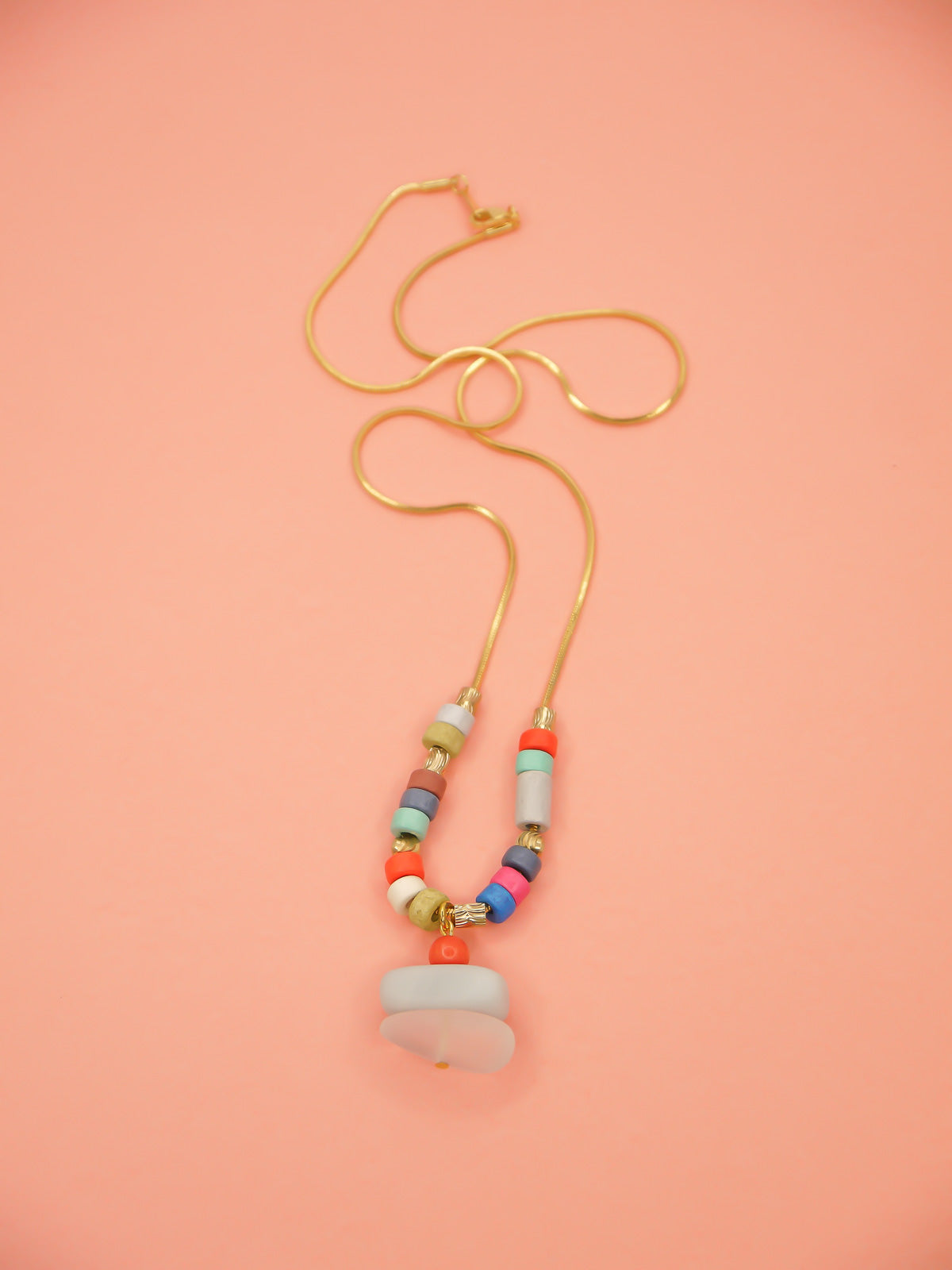 Crystal gemstone pendant necklace with a frosted crystal bead, stacked with an amazonite and coral bead, featuring multi coloured ceramic tube beads with textured brass tube beads hung on a gold plated snake chain