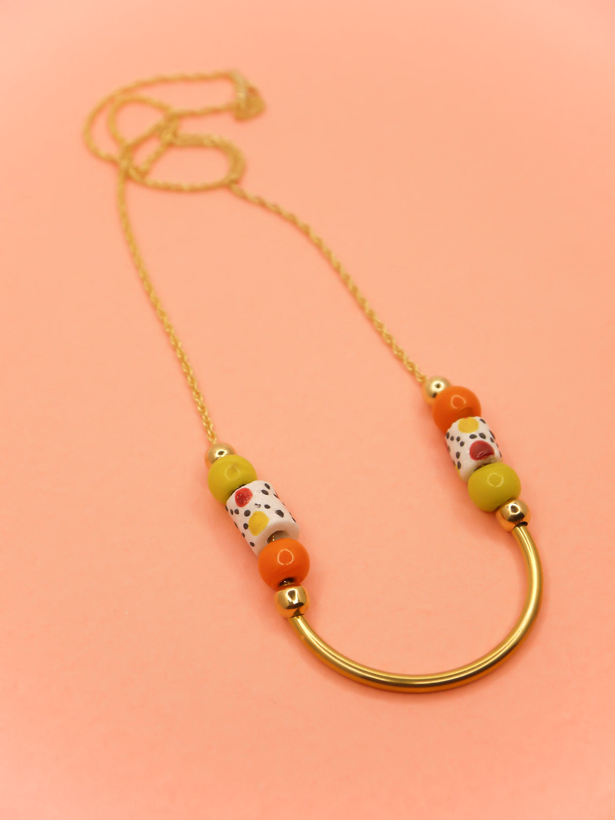 Lightweight beaded necklace with a brass curved bar in the centre and brass ball beads with orange & chartreuse ceramic ball beads and white spotted tube ceramic beads strung on both sides with a 24k gold plated snake chain