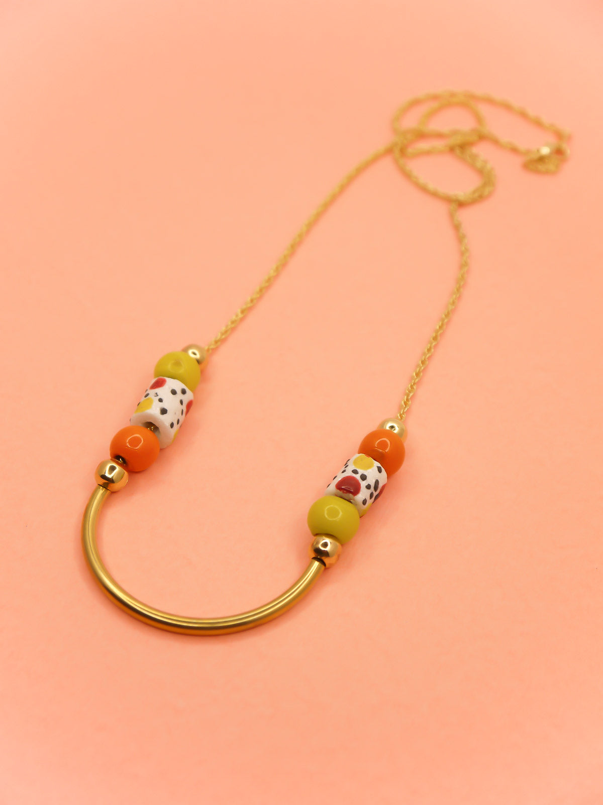 Lightweight beaded necklace with a brass curved bar in the centre and brass ball beads with orange & chartreuse ceramic ball beads and white spotted tube ceramic beads strung on both sides with a 24k gold plated snake chain