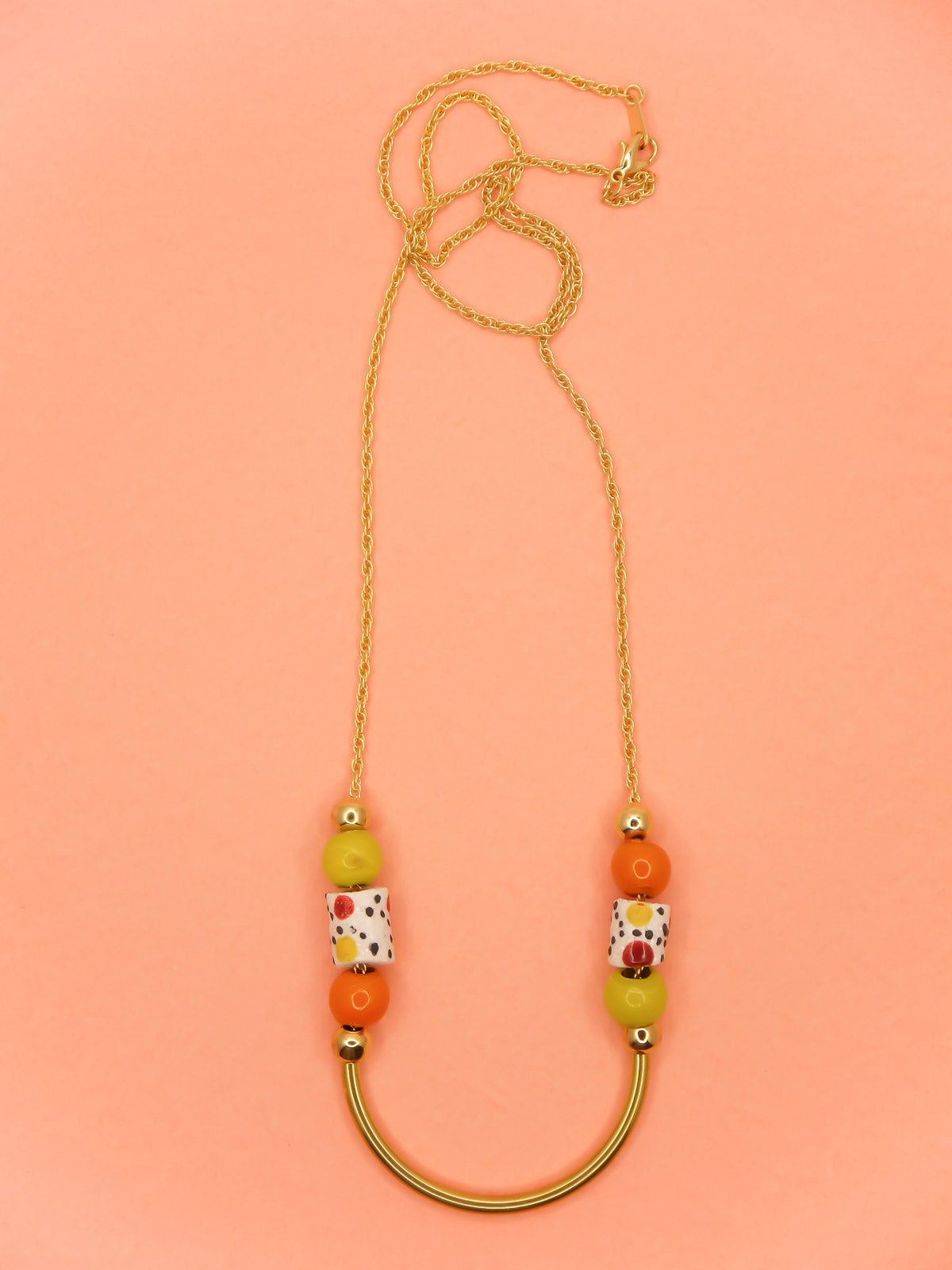 Lightweight beaded necklace with a brass curved bar in the centre and brass ball beads with orange & chartreuse ceramic ball beads and white spotted tube ceramic beads strung on both sides with a 24k gold plated snake chain