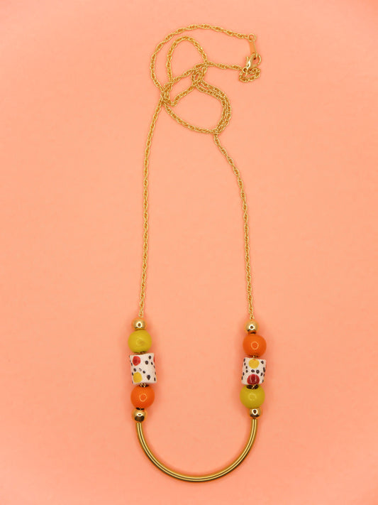 Lightweight beaded necklace with a brass curved bar in the centre and brass ball beads with orange & chartreuse ceramic ball beads and white spotted tube ceramic beads strung on both sides with a 24k gold plated snake chain