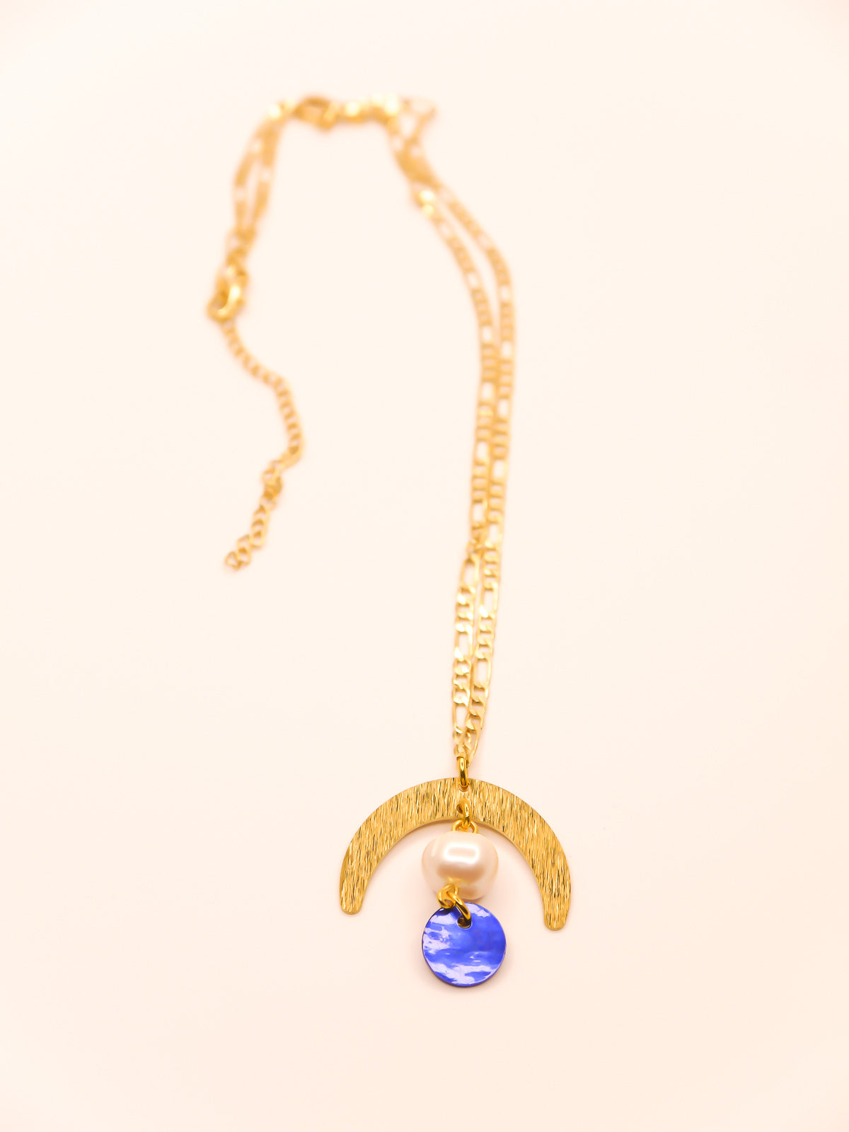 Geometric lightweight pendant necklace with a textured brass arch semi circle with a pearl and blue round shell disk hung from the arch on a faceted gold curb chain with extender.