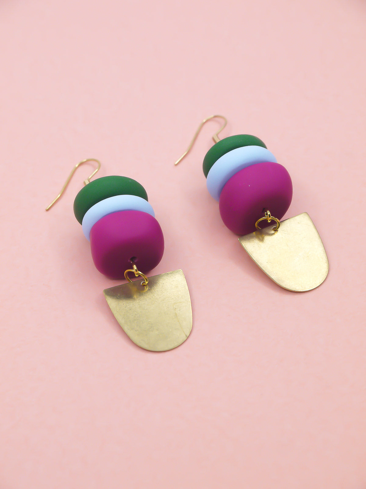 Colourful beaded earrings in green, blue & pink with gold accents on a pink background