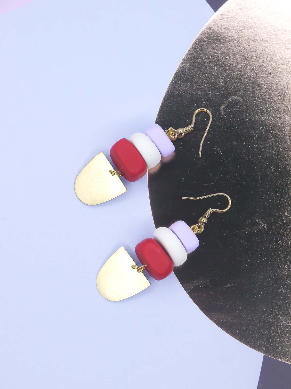 Colorful earrings with geometric shapes on a light blue & gold background