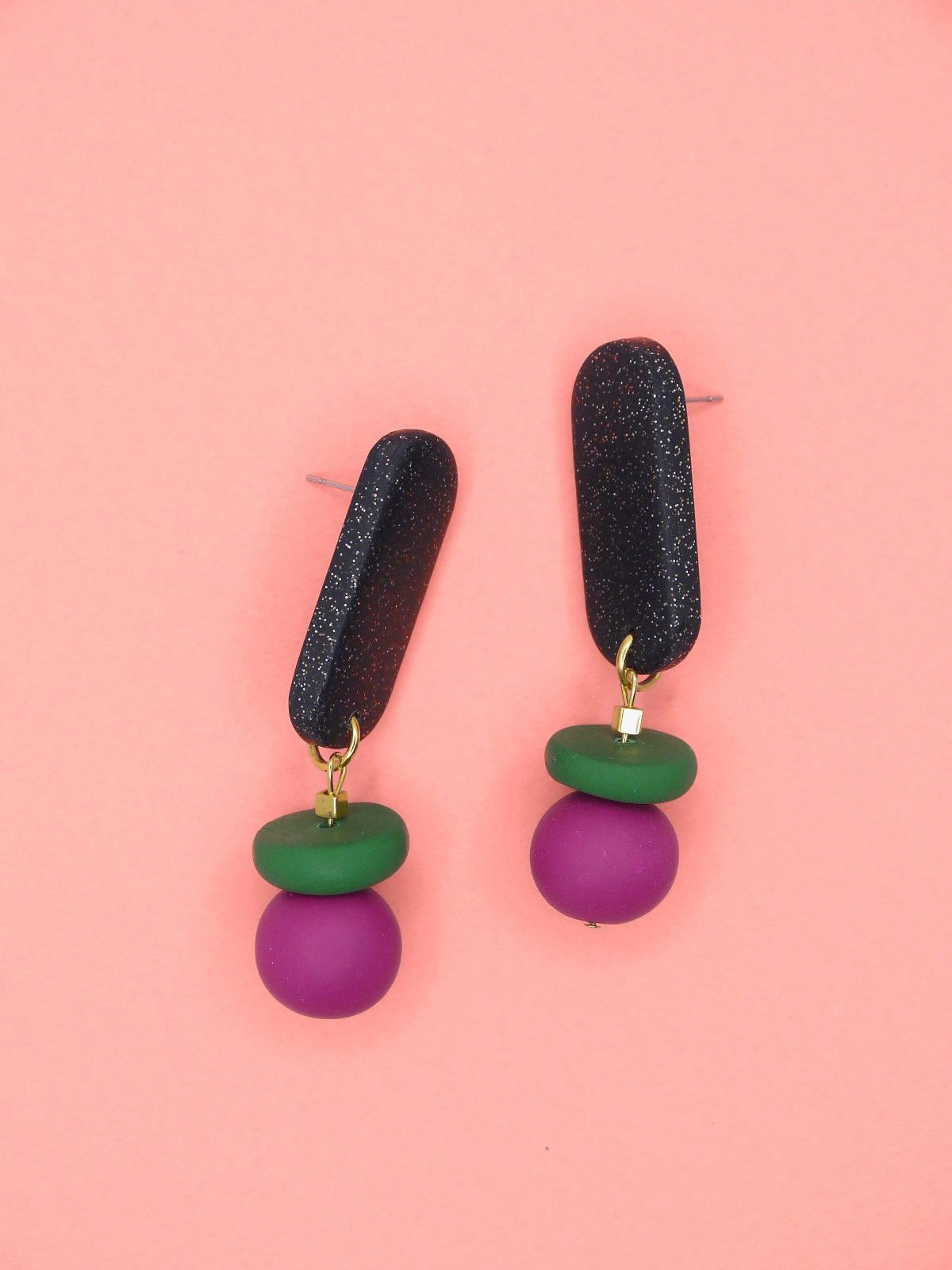 Pair of earrings with black, green, and pink beads on a pink background