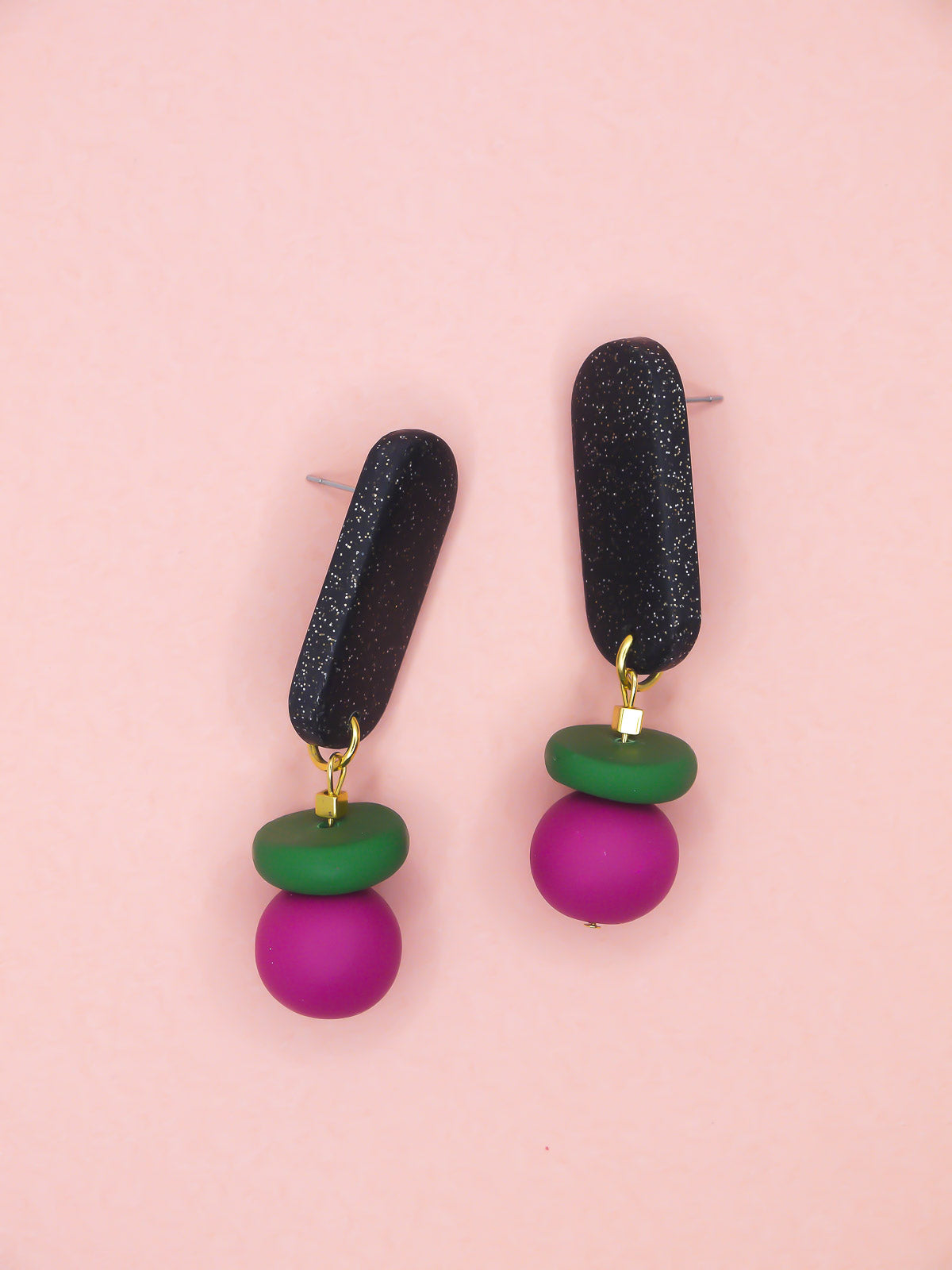 Pair of earrings with black, green, and pink beads on a pink background